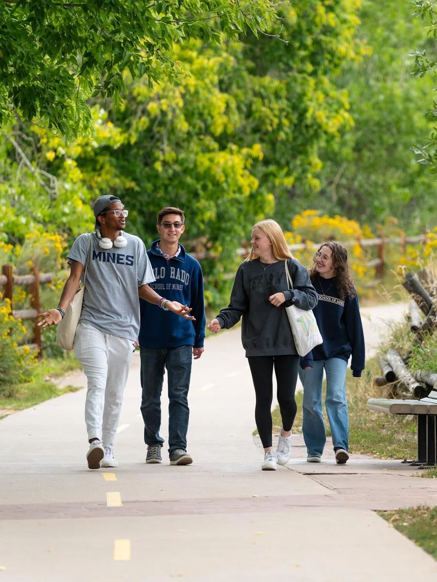 Four new Mines undergraduate students walk along a path discussing engineering class assignments.