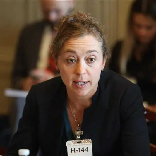Elizabeth Holley speaking at a meeting, wearing a black blazer and a name tag labeled 
