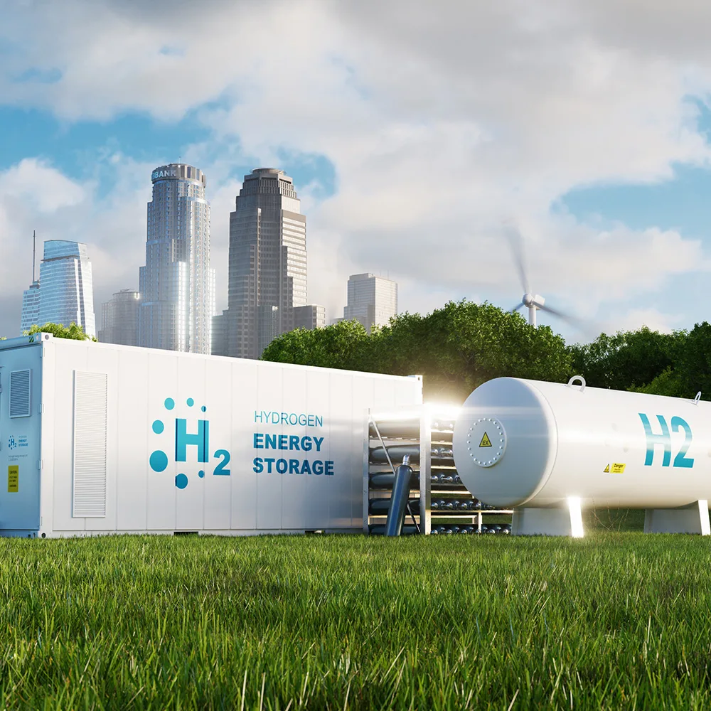 Hydrogen energy storage unit and tank on grass with city skyline and wind turbine in the background under a partly cloudy sky.