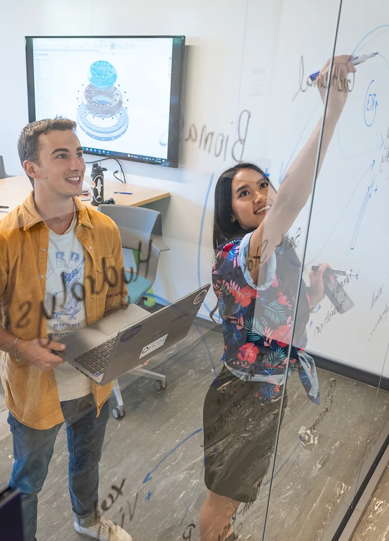 Mines students brainstorming on a glass wall with markers