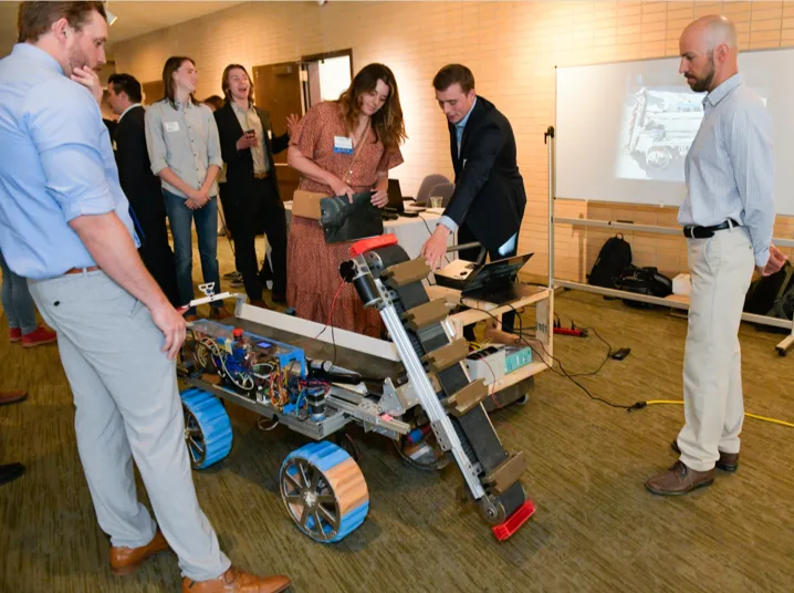 A group of students displaying their student-built engineering project of a Mars rover prototype