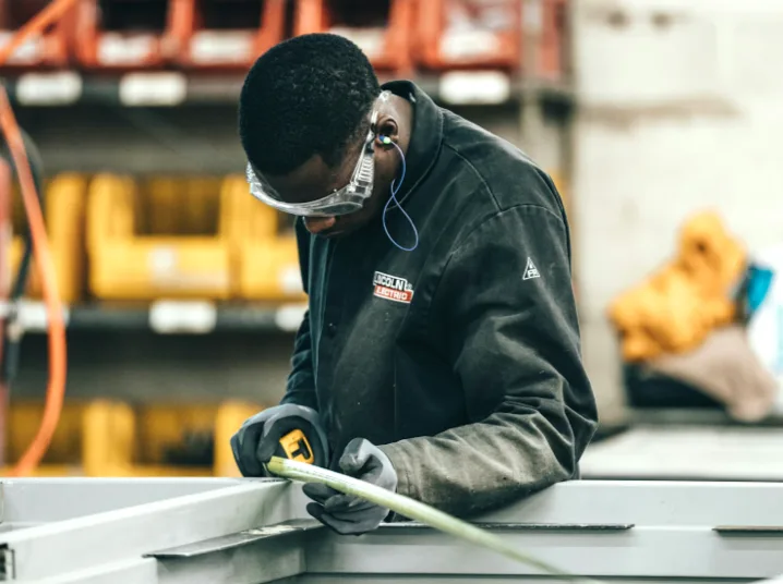 A technician measuring metal components while wearing protective equipment