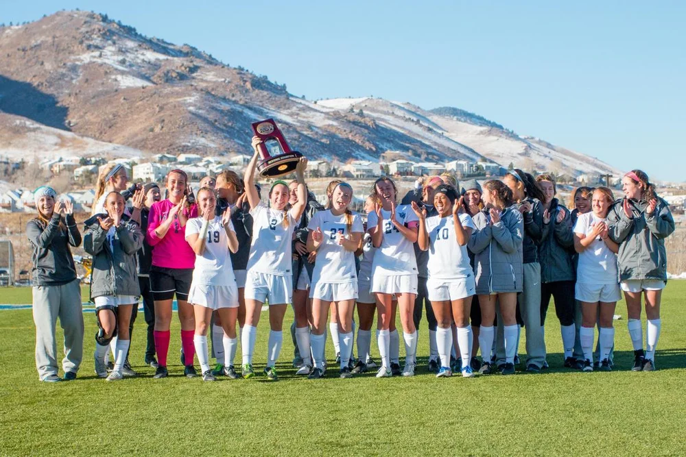 Colorado School of Mines women's soccer team poses at the Clear Creek Athletic Complex holding up a championship trophy.