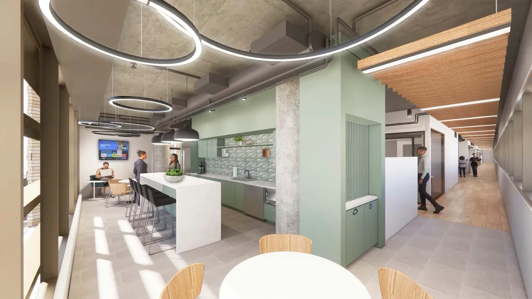 Modern office kitchen and lounge area with large windows, circular ceiling lights, high bar stools, and people interacting in a bright, open space.
