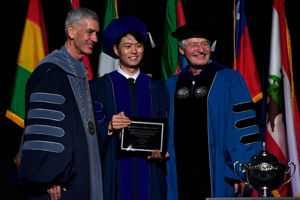 PhD graduate holds plaque standing between Mines President and Mines Vice President for Research