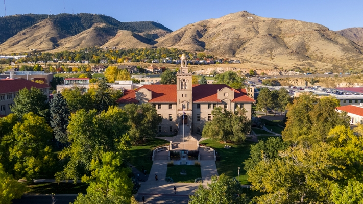 Aerial view of Guggenheim building surrounded by trees, set against a backdrop of dry, rolling hills under a clear blue sky.