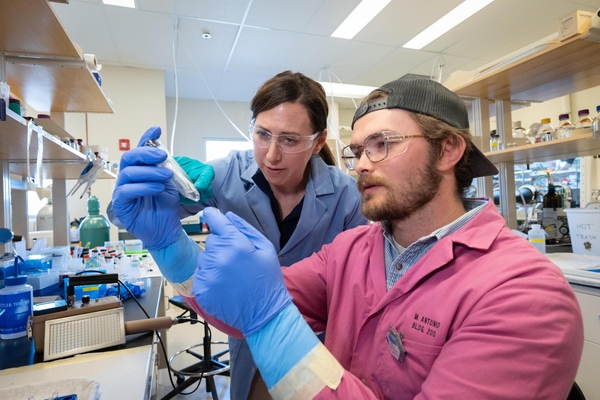 Jenifer Shafer and a graduate student wearing protective gear closely inspect a small plastic tube in a radiochemistry laboratory.