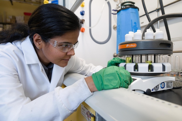 Ramya Kumar in white lab coat and green gloves inspecting item in the lab