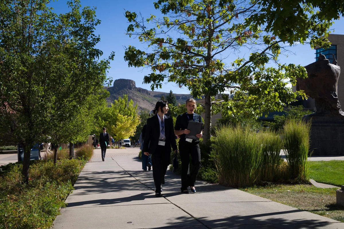 Two students in business wear walk across campus with South Table Mountain in the background