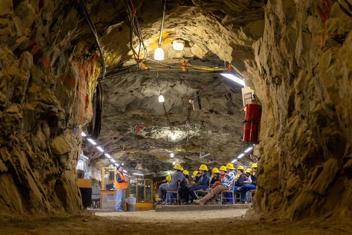 Students in yellow hard hats sit at desks in a classroom hewn out of a mine