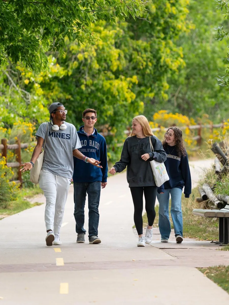 Four new Mines undergraduate students walk along a path discussing engineering class assignments.