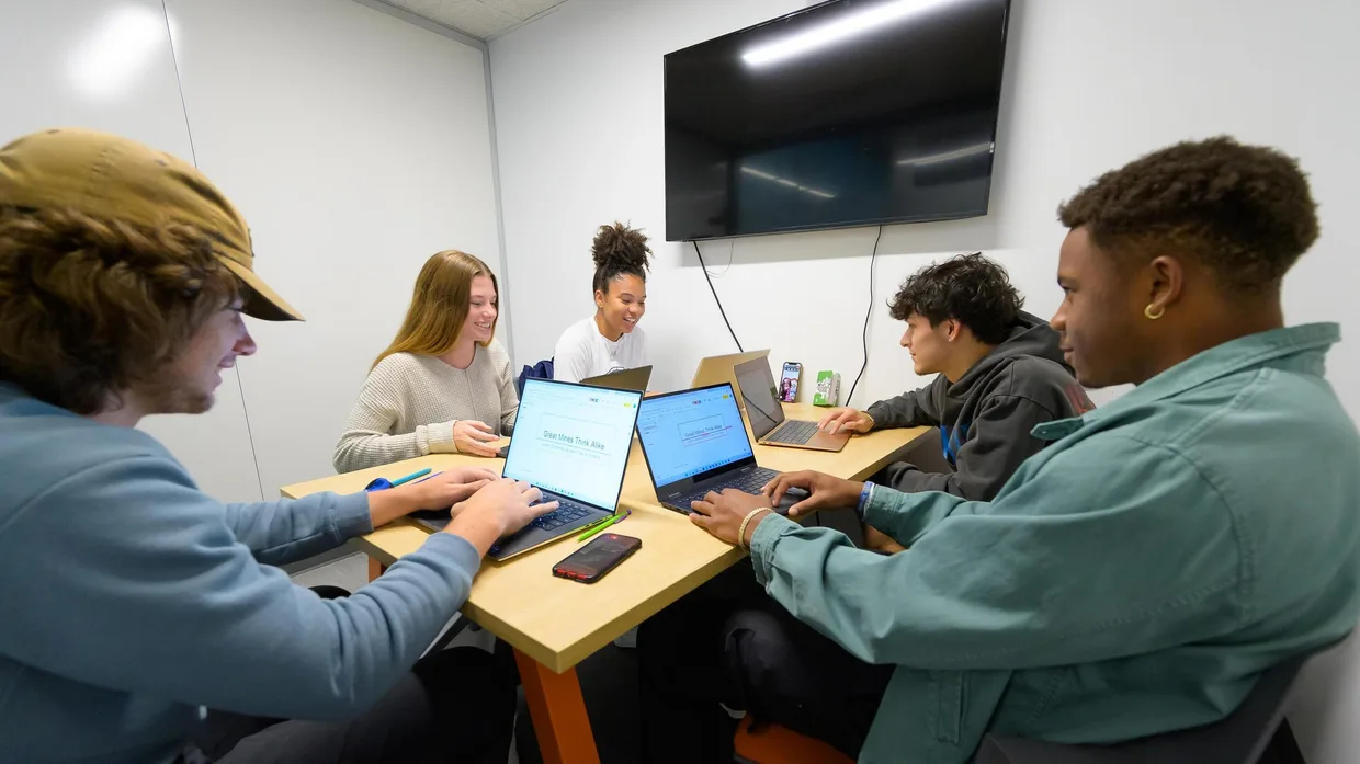 Undergraduate students sit at a table with laptops while collaborating in a breakout room on an engineering project.