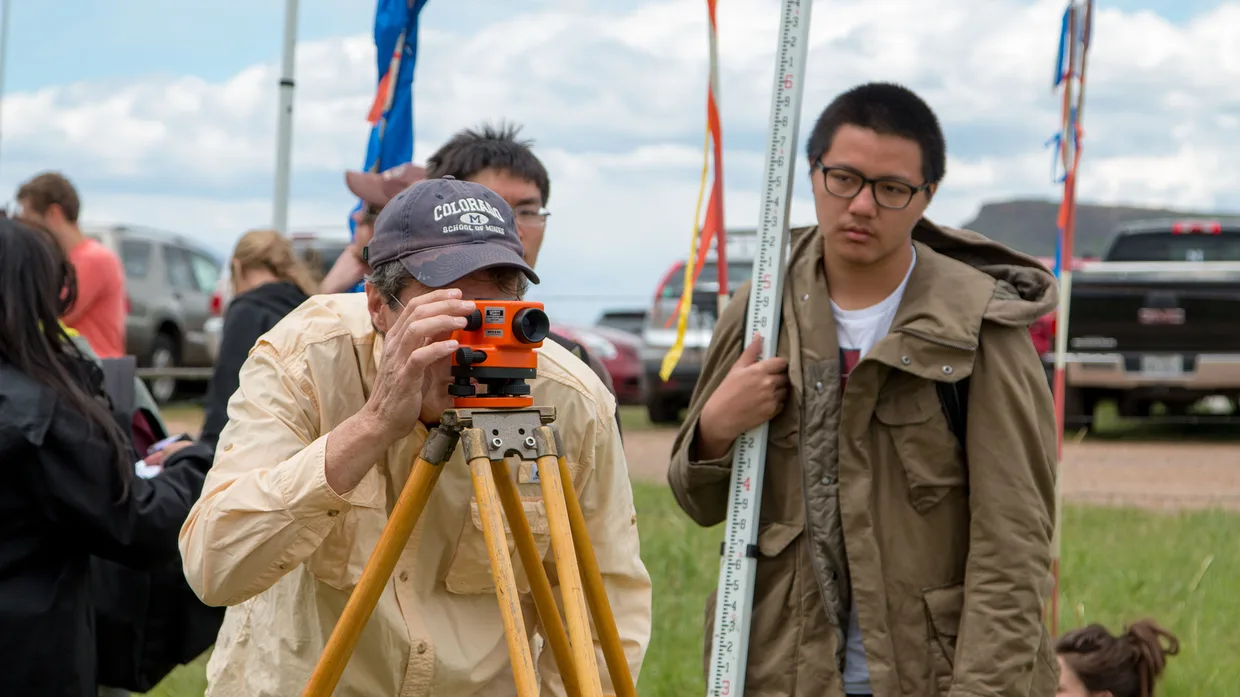 A group of people standing around a man using a theodolite.