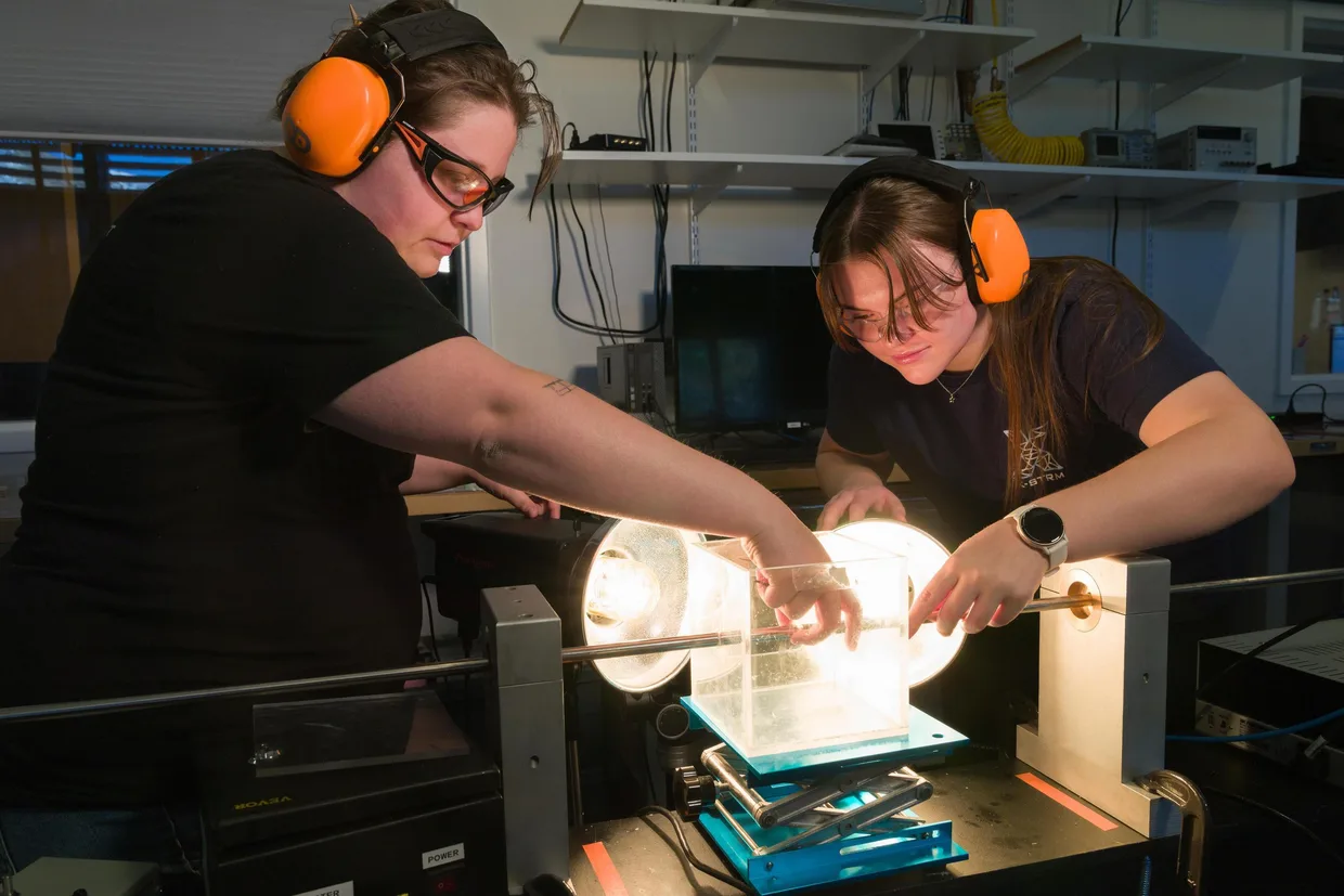 Two students wearing orange protective earmuffs work on experiment in materials lab