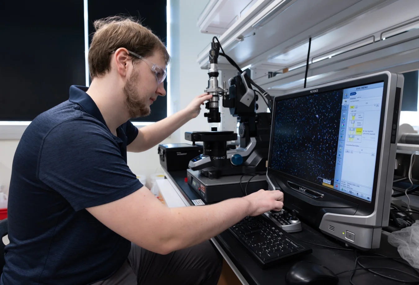 A Mines student The researcher is operating a Keyence VHX series digital microscope, identifiable by its distinctive control console and monitor display.