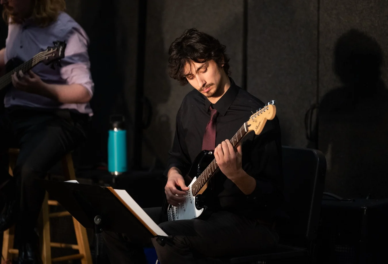 Mines Student focused on playing a Squier electric guitar during a live performance