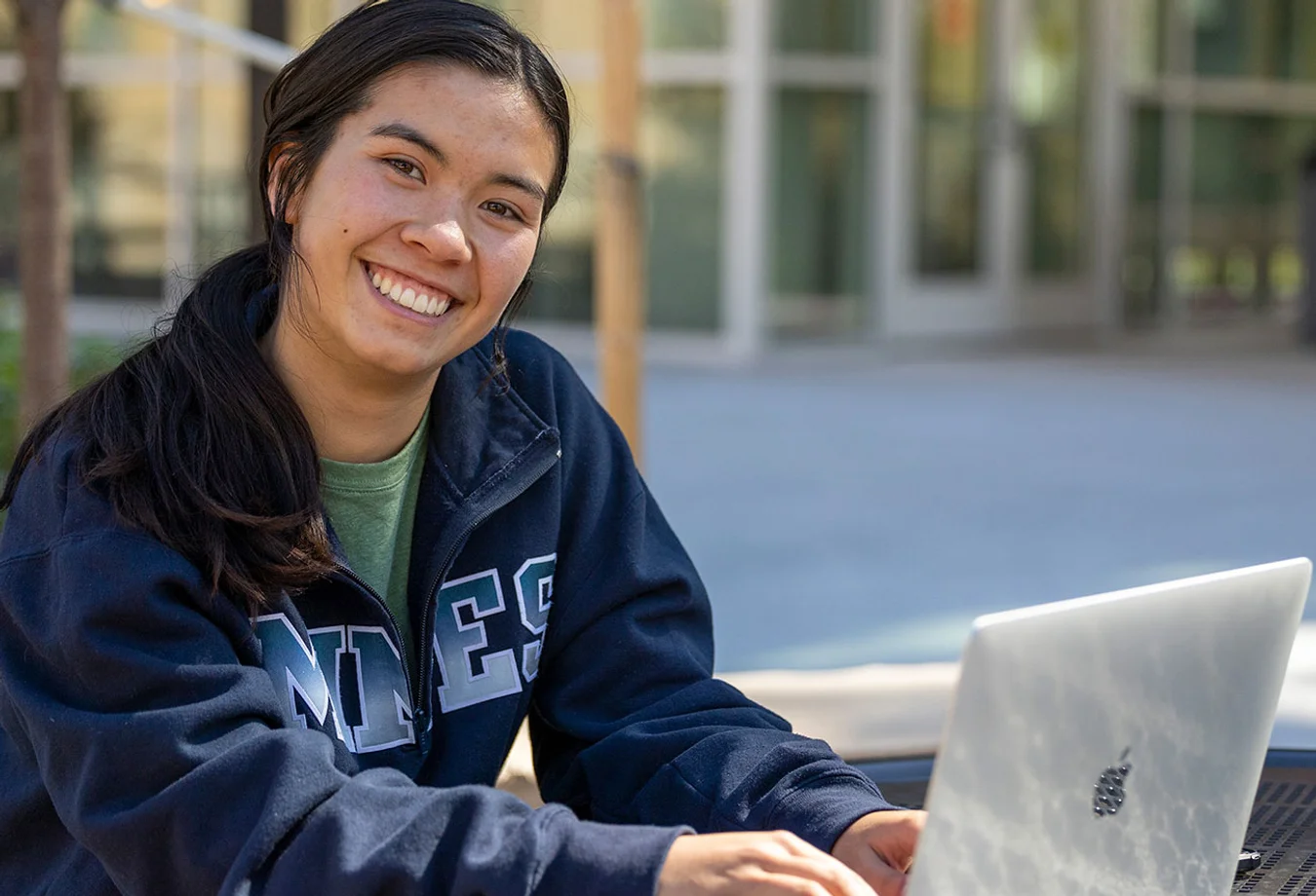 Female Mines student working on a laptop outside a building on campus