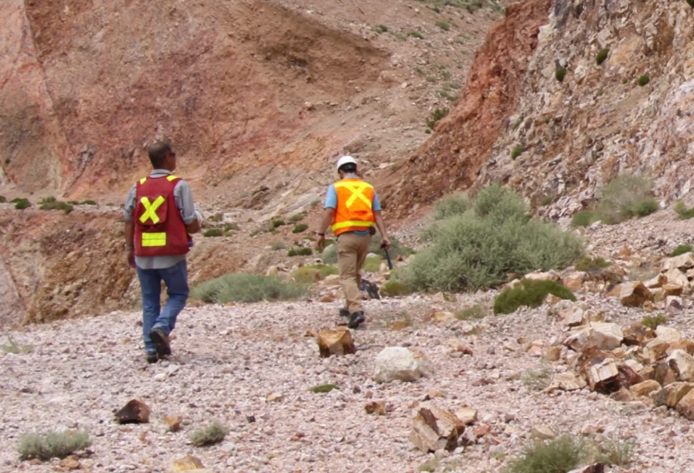 two people walking down a rocky path in the desert.