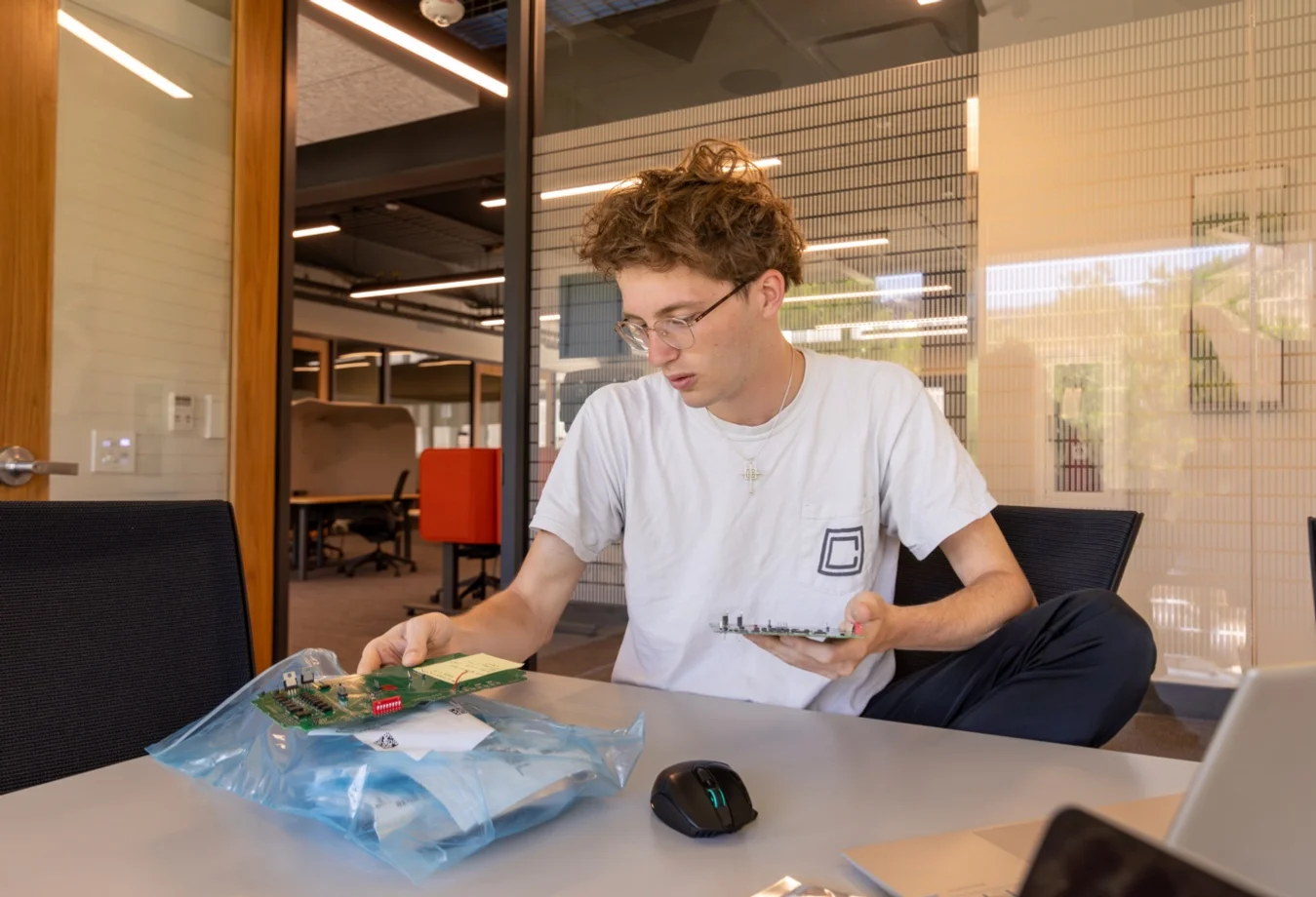A male student sitting in a conference room looking at a circuit board.