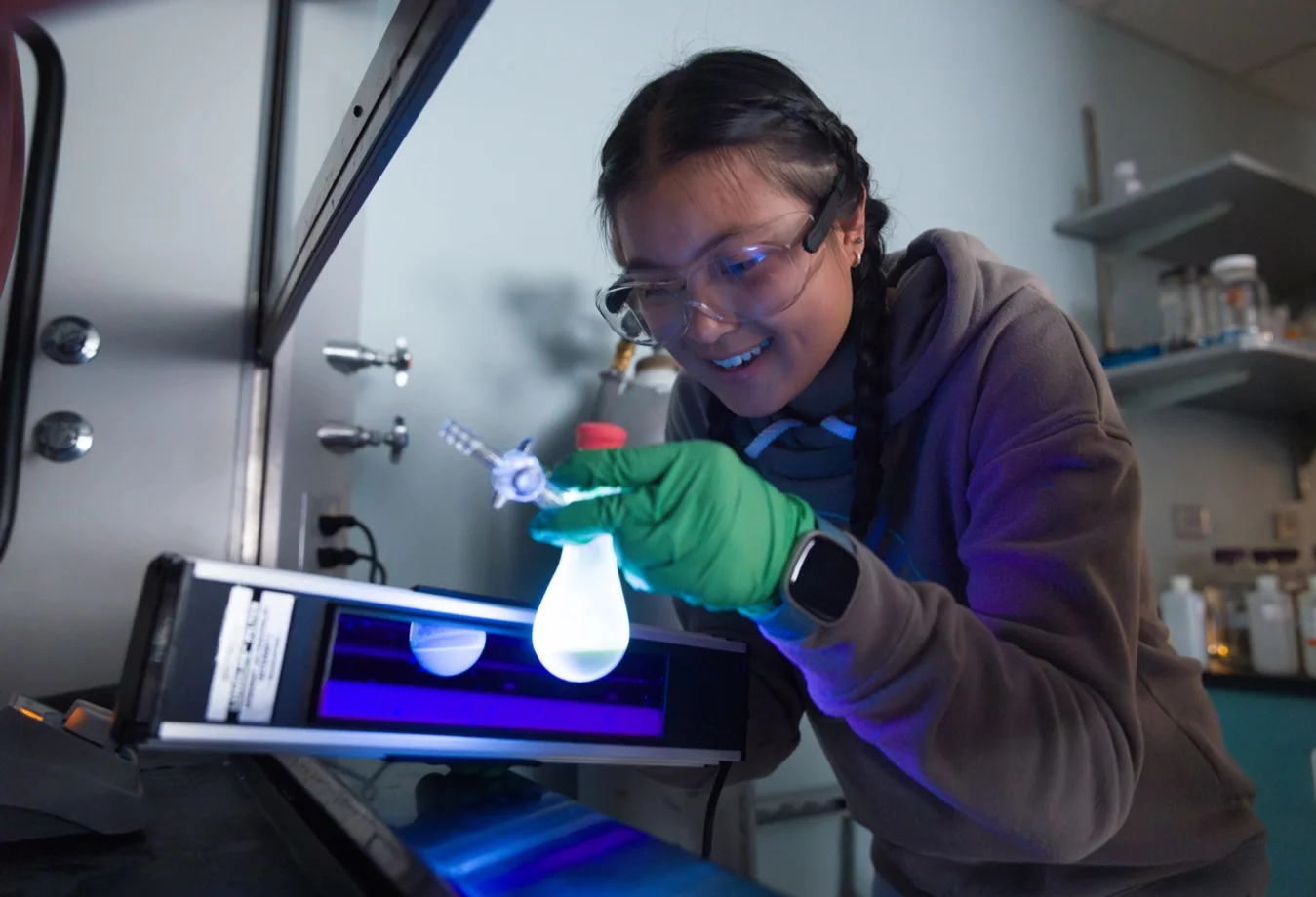 A researcher holding a glowing flask filled with a catalyst designed for organic photoredox reactions