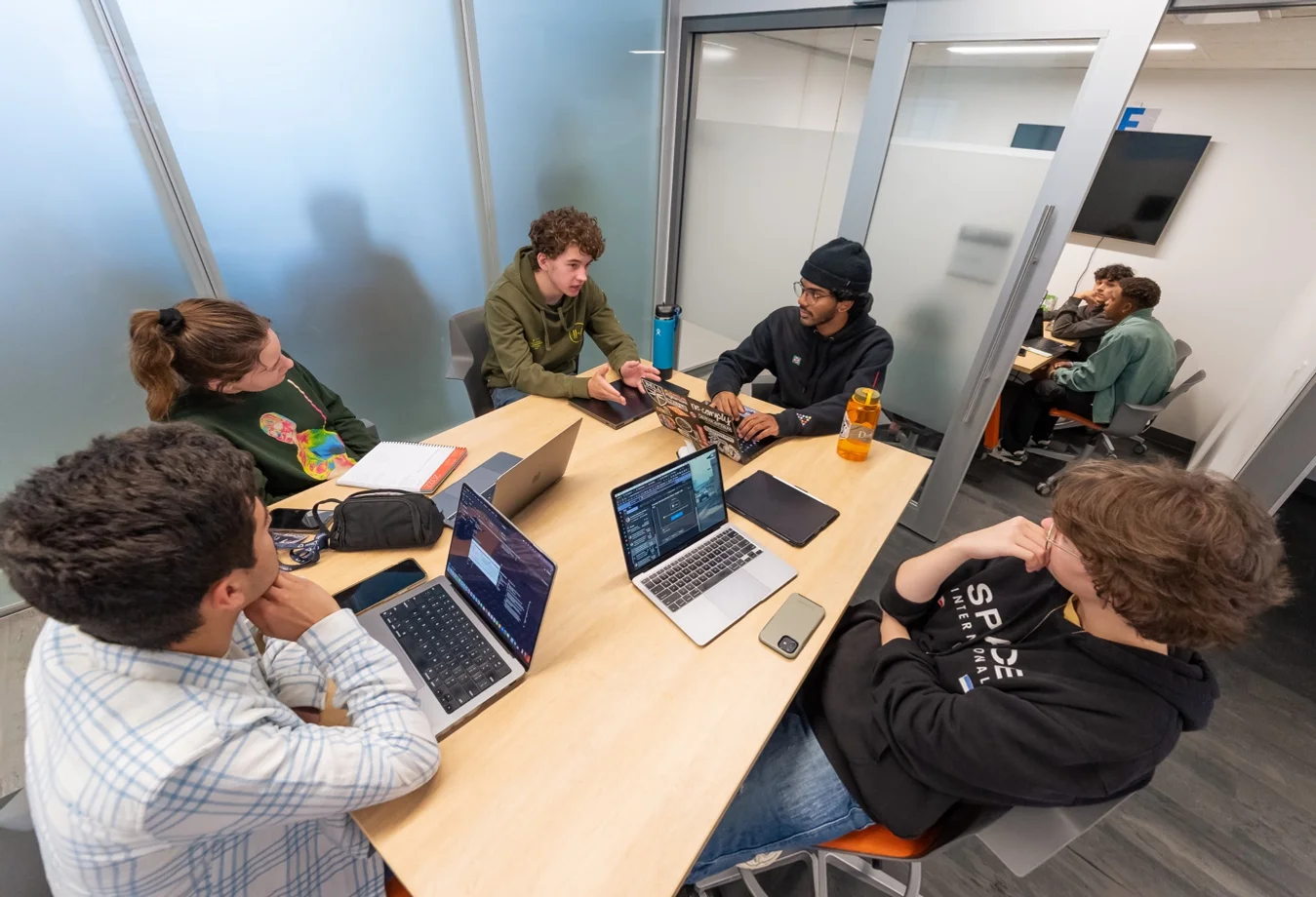 A group of mines students sitting in a conference room collaborating on a project with their laptops open.