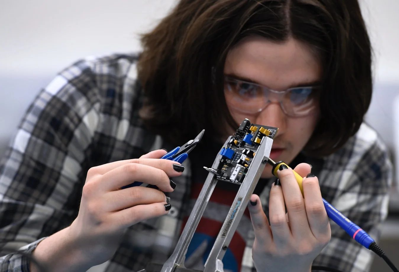A Mines student focused on assembling a small circuit board component in the laboratory