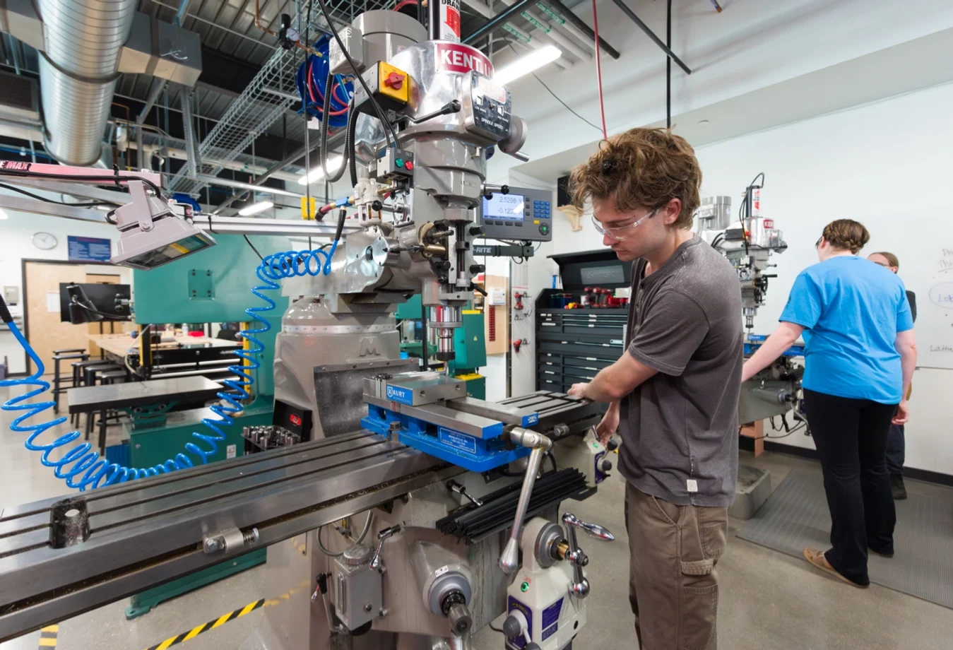 A male Mines student is operating a Kent USA manual knee mill in the machine shop.