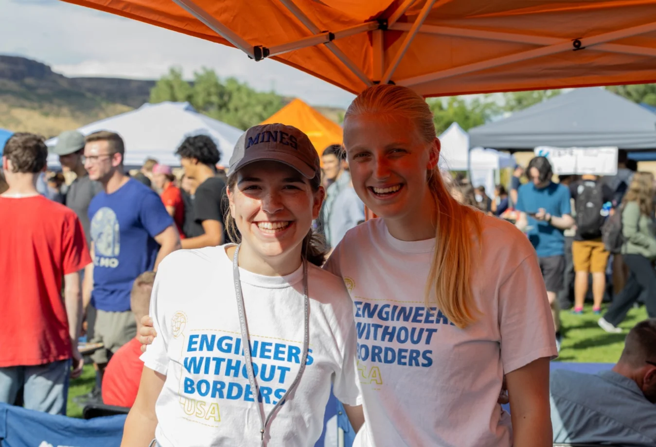 To female students wearing white Engineers Without Borders USA t-shirts at an outdoor event.