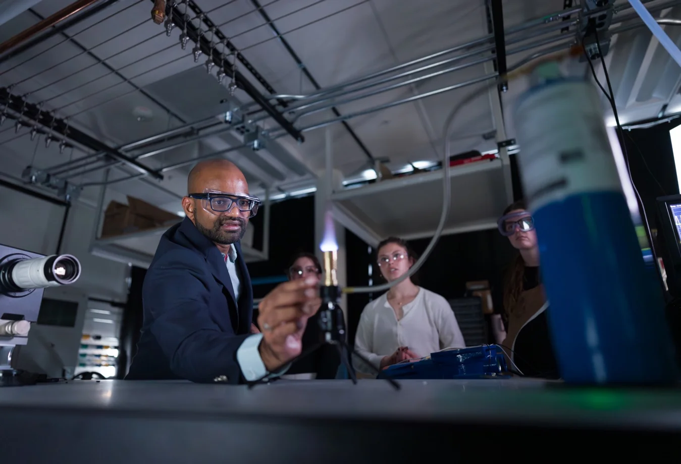 A male professor guiding students through a chemistry experiment using a Bunsen burner
