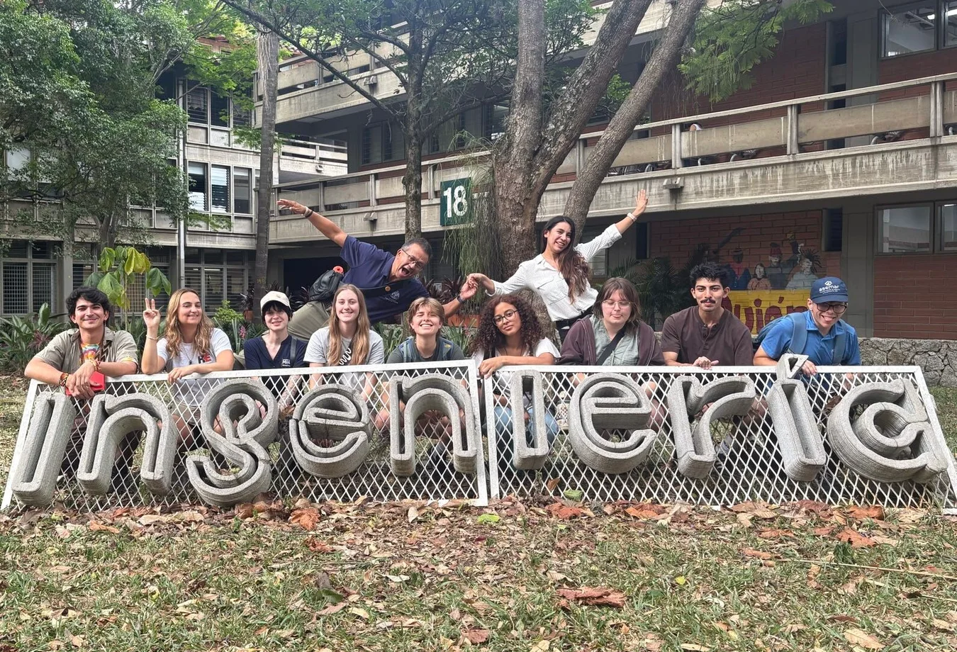 Group of students posing behind a large “Ingeniería” sign outside a campus building.