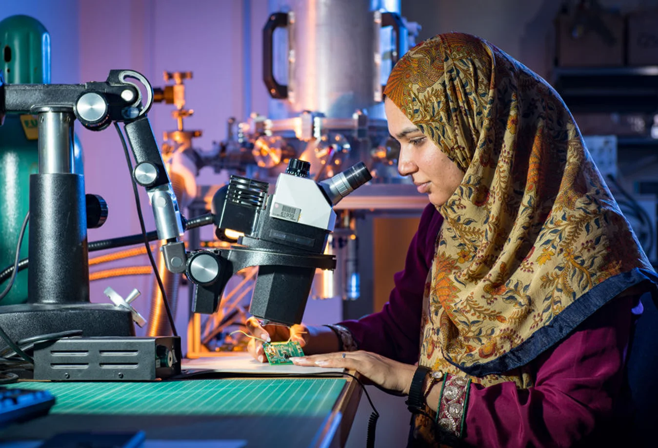 A woman in a headscarf looking through a microscope.
