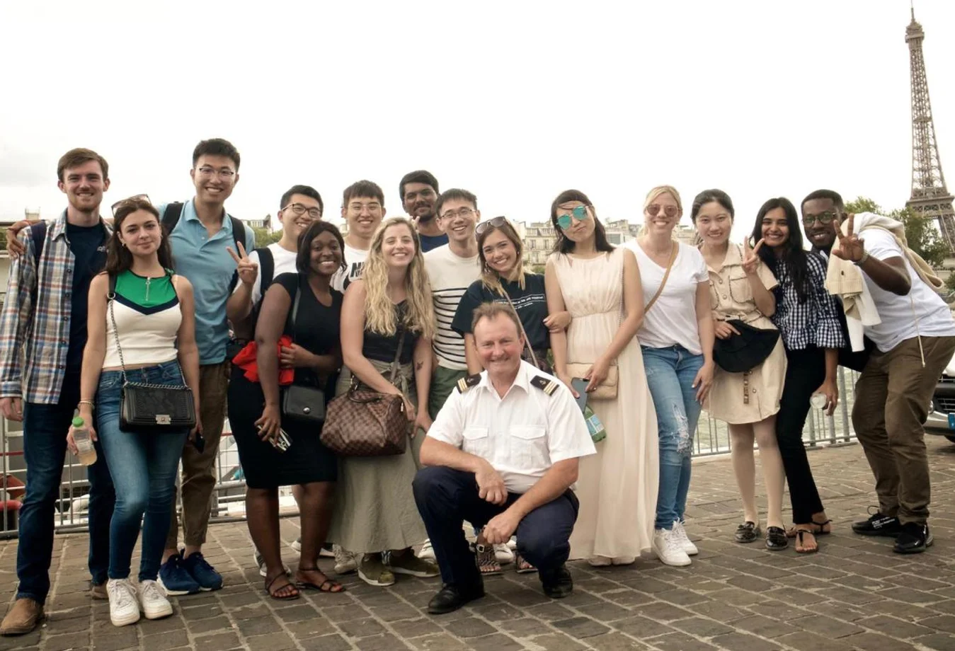 Group of Mines students and a uniformed man posing near the Eiffel Tower on a cloudy day.