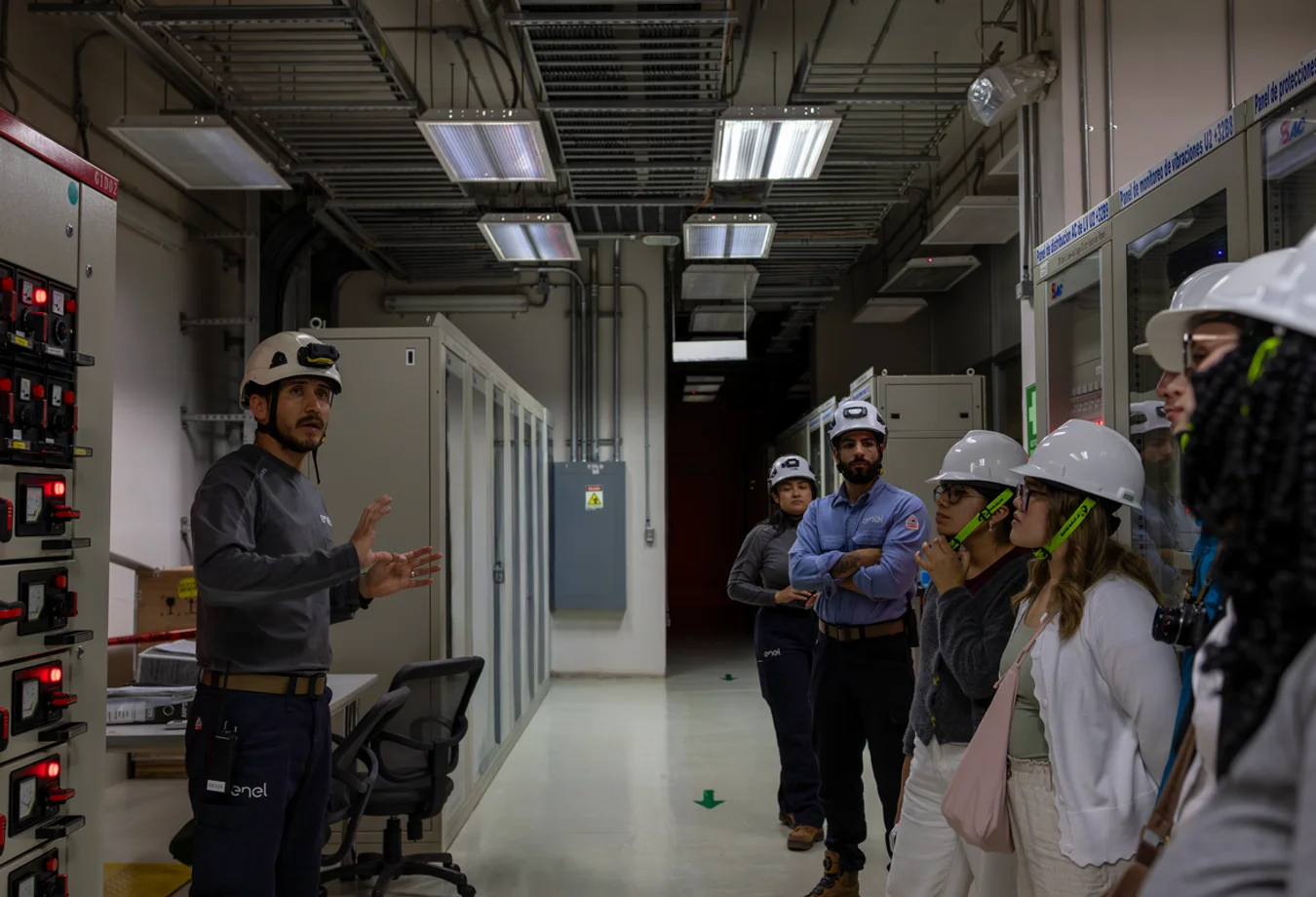 A group of Mines students and project leader wearing hard hats stands together in a room, discussing a construction project.