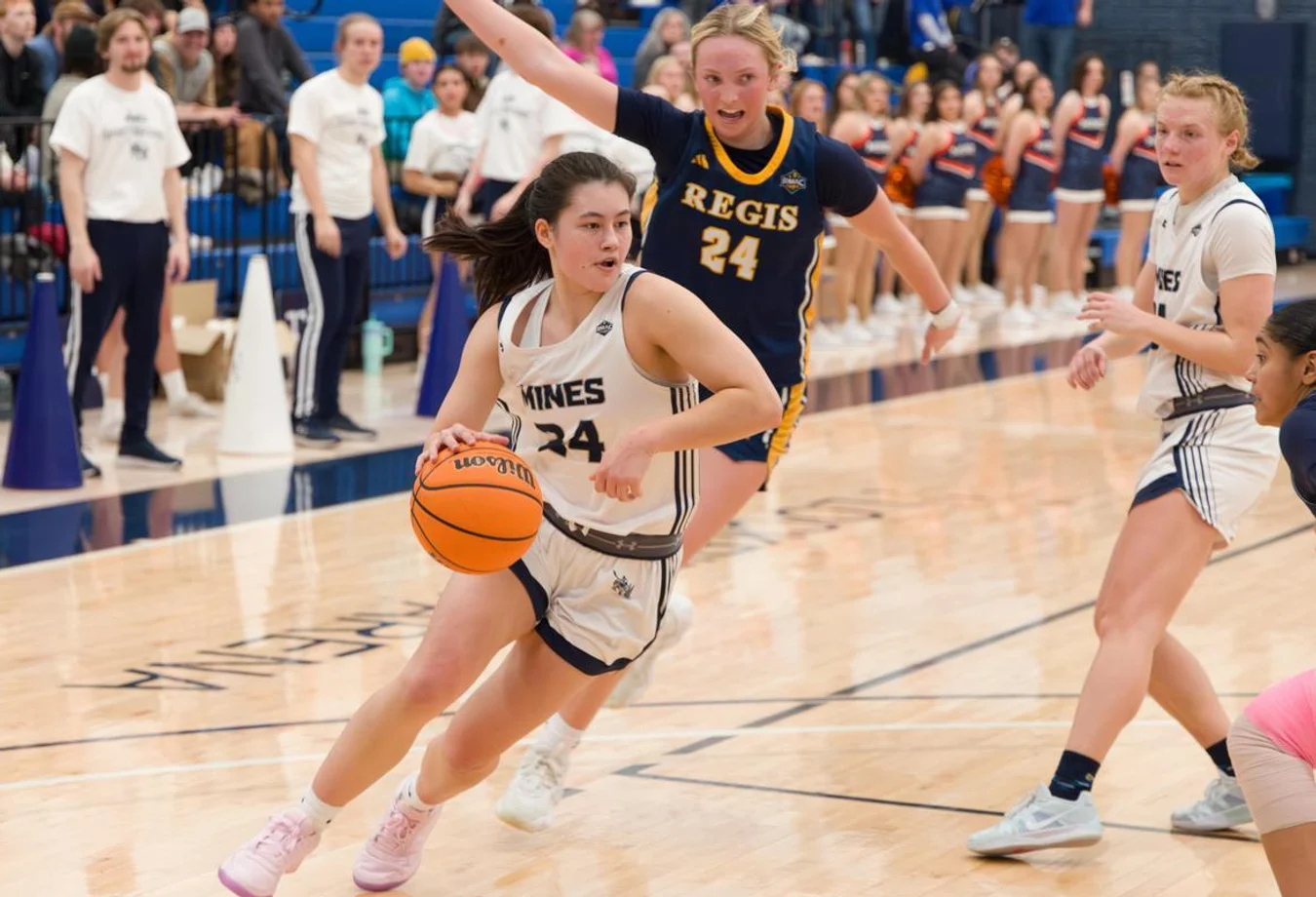 Mines women's basketball athlete dribbling the ball on court through the opposing team's defense.