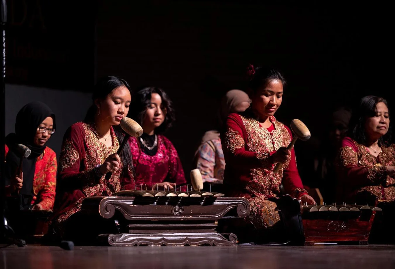 Women in traditional attire play the gamelan, an Indonesian percussion instrument, in a focused cultural music performance.
