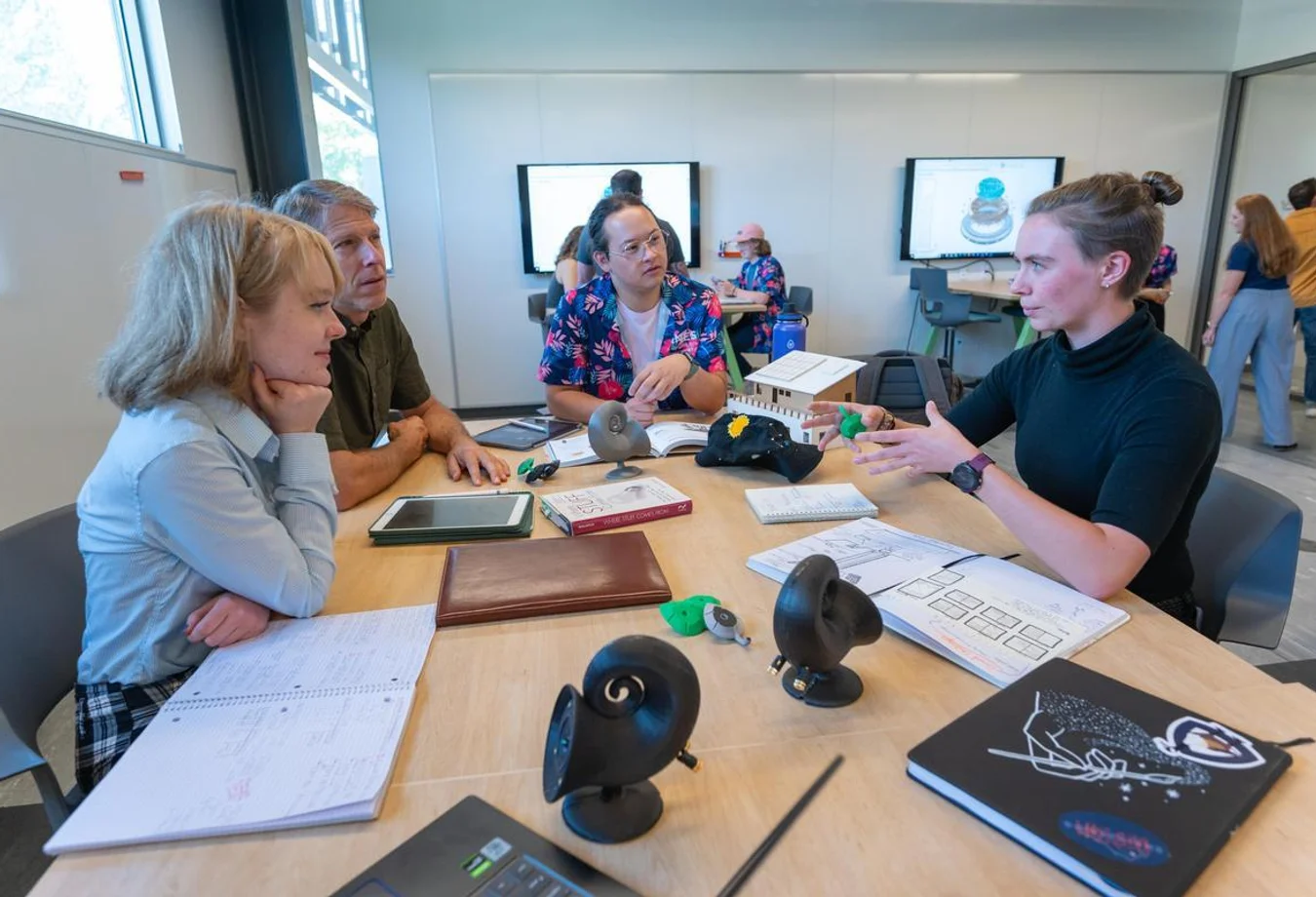 A team of Mines students sit around a table discussing an engineering project showcasing professional communication skills.