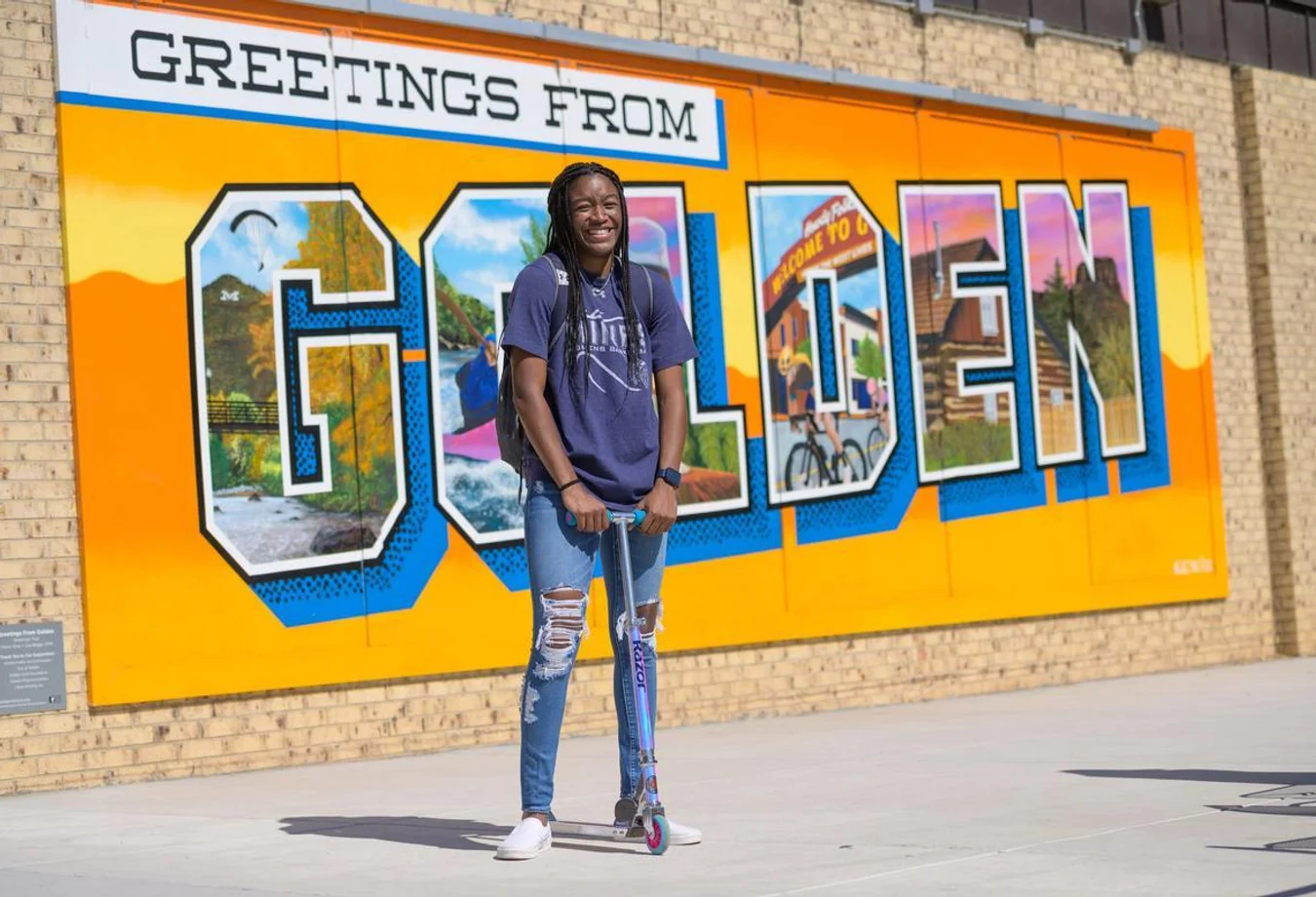 Mines student with a scooter in front of the Welcome to Golden sign