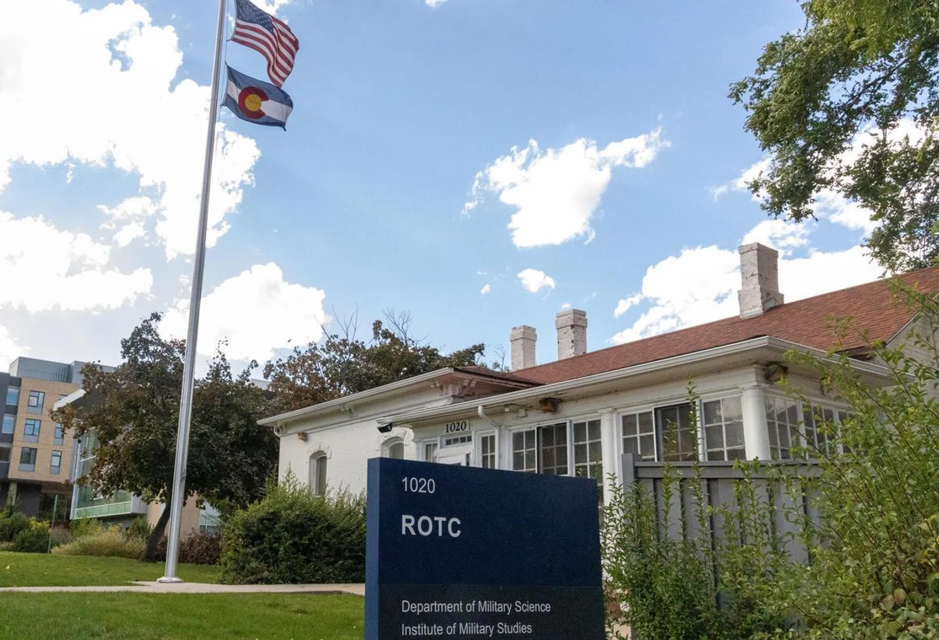 ROTC building at 1020 with American and Colorado flags flying on a sunny day with scattered clouds and surrounding greenery.