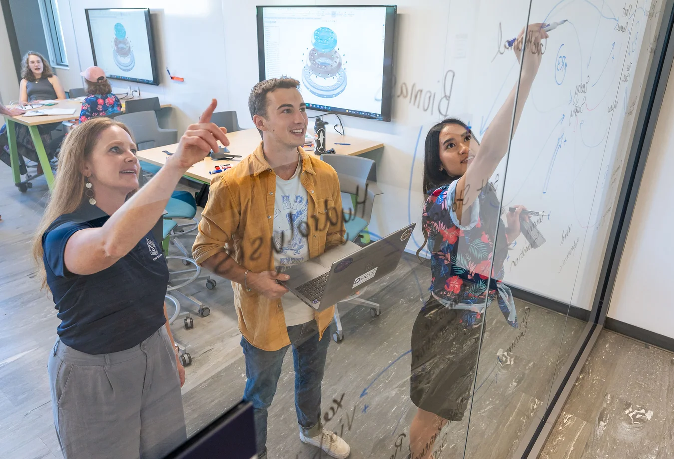 A group of people standing in front of a whiteboard in a classroom.