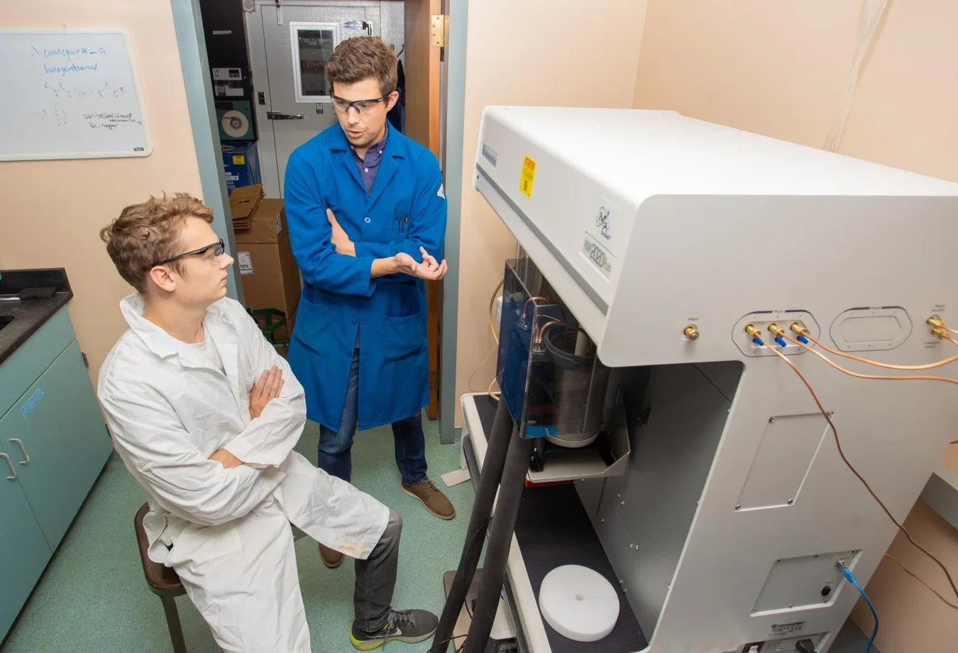Two men in lab coats standing next to a machine.