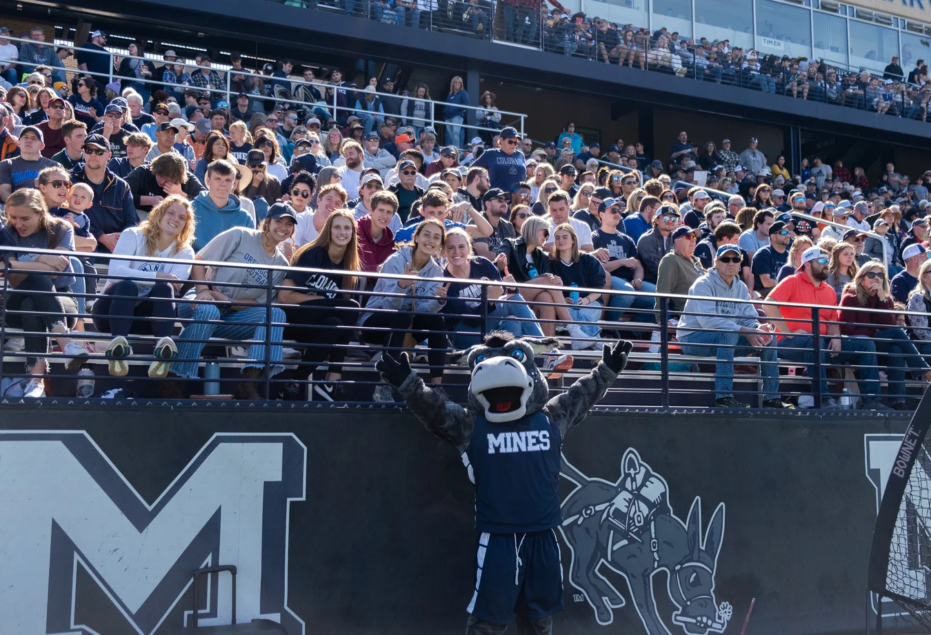 Crowd of fans in stadium stands with a mascot dressed in 