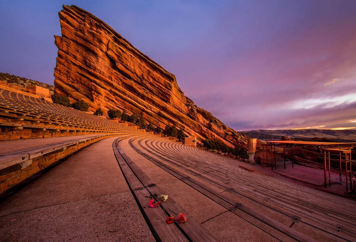 Red Rocks amphitheater empty at sunset with curved wooden benches and a large red rock formation in the background.