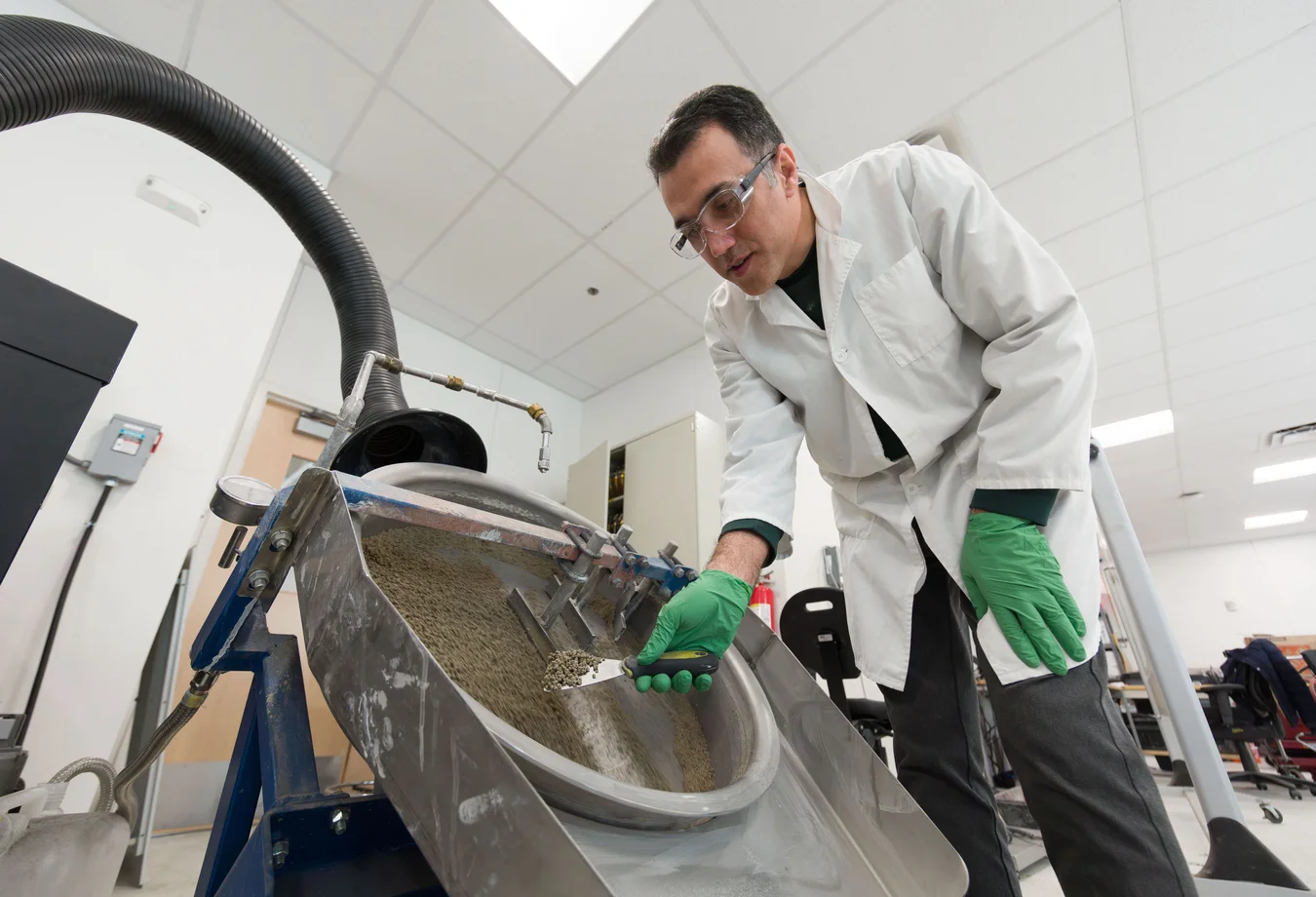 A man in a lab coat and green gloves working on a machine.