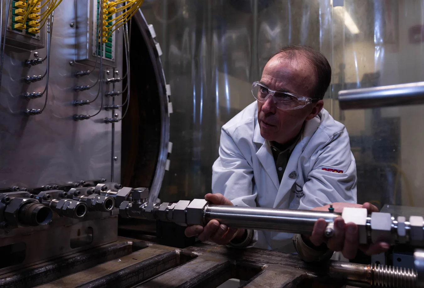 A man in a lab coat and goggles working on a machine.