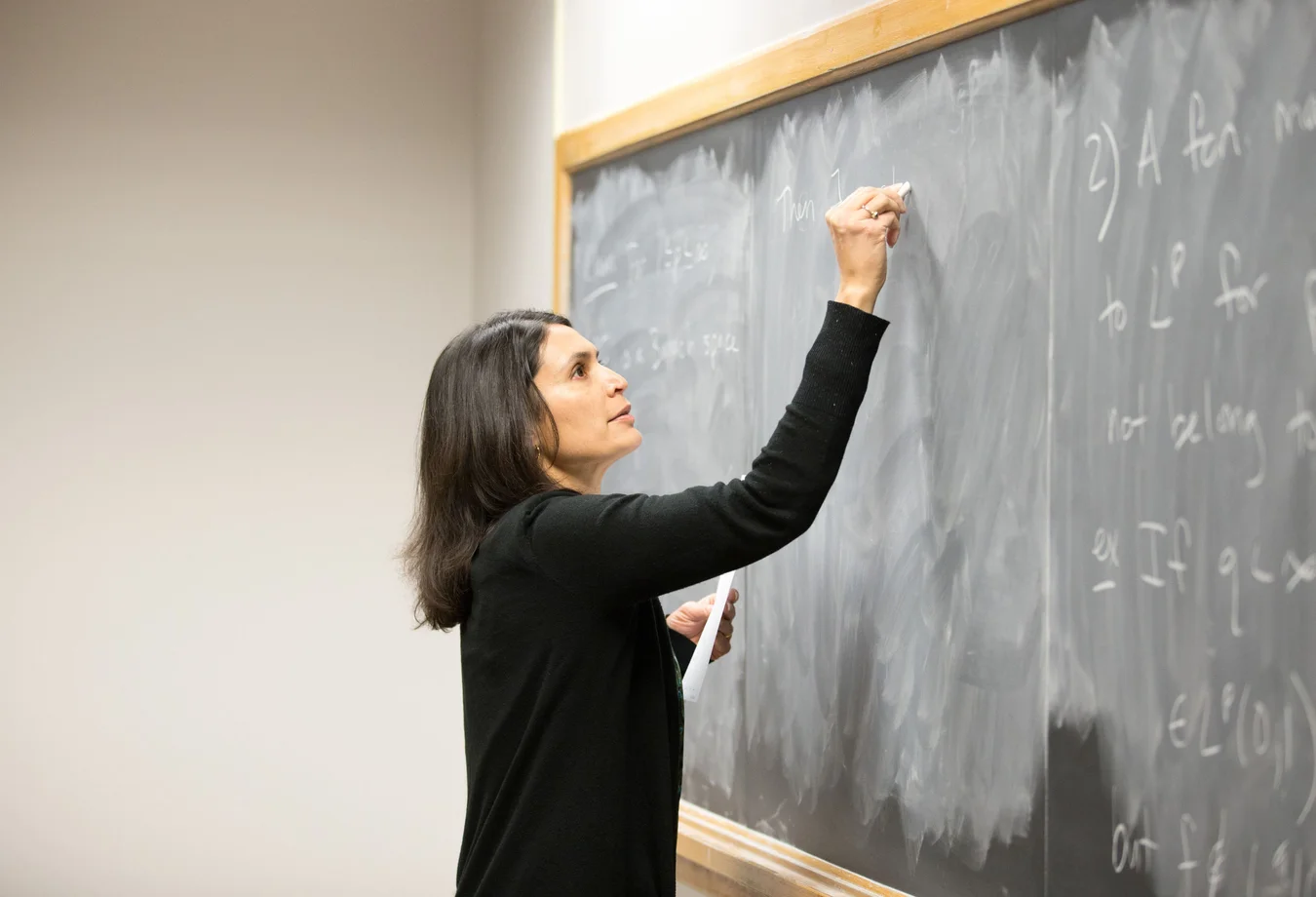 A woman writing on a blackboard in a classroom.