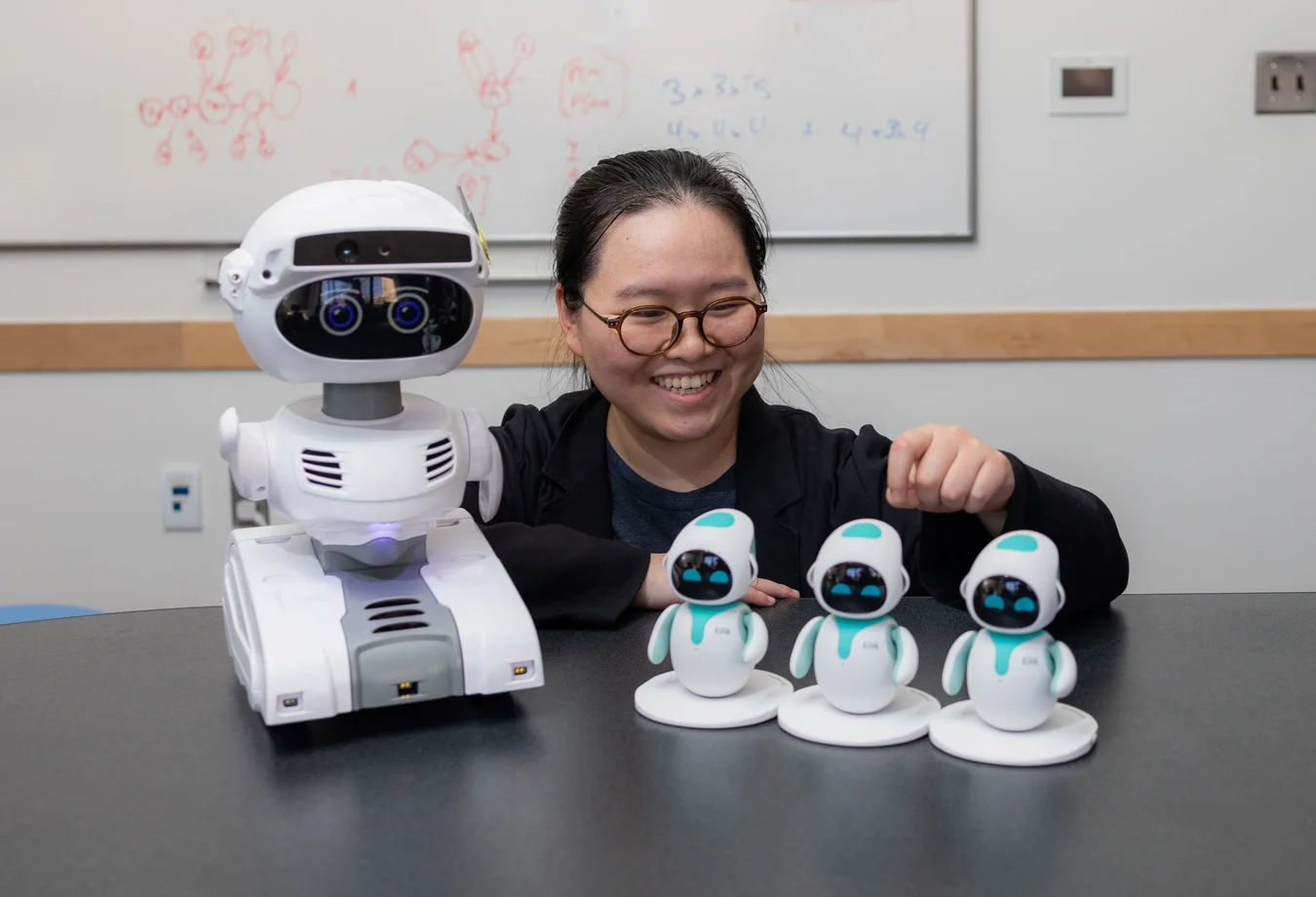 A woman sitting at a table with three robots in front of her.