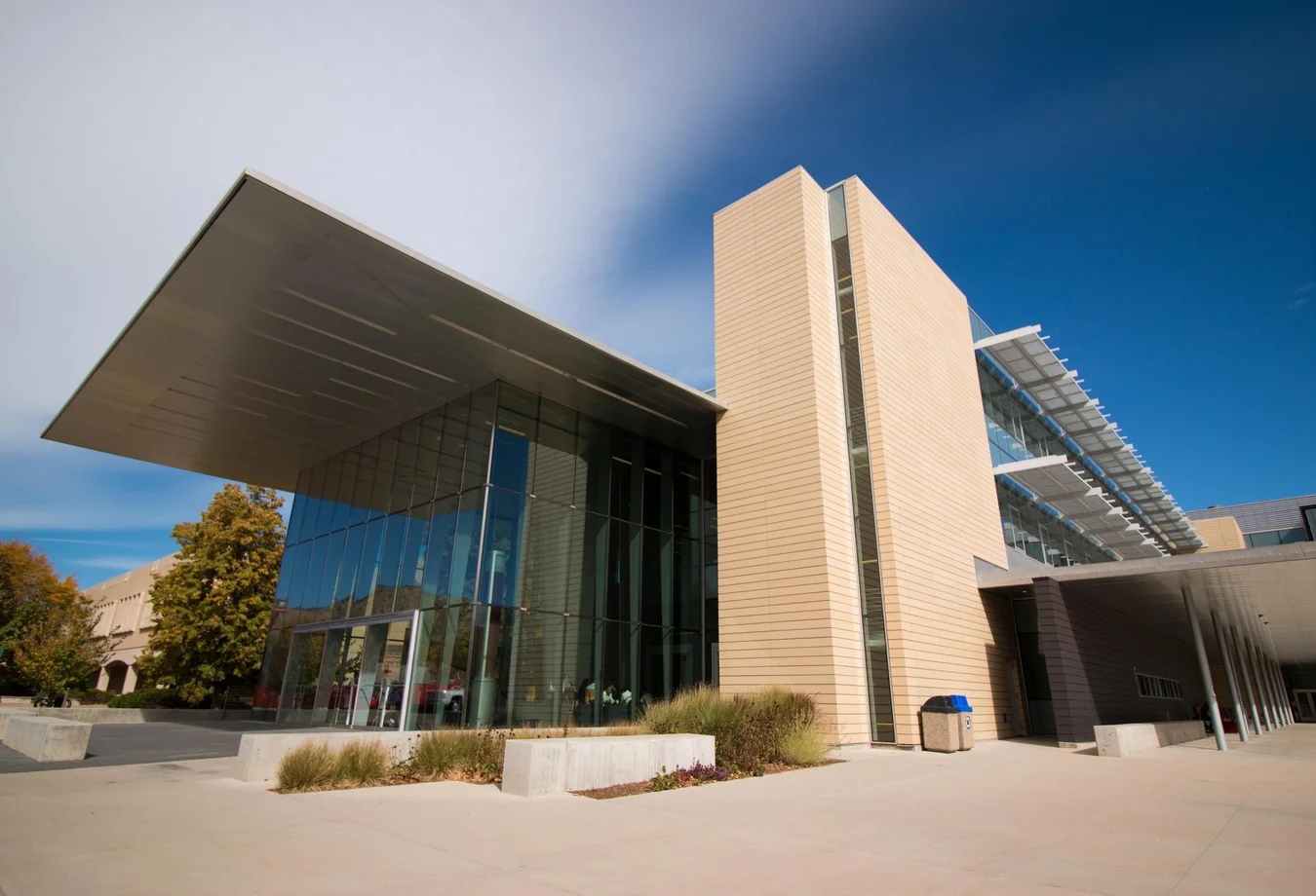 A modern building featuring a prominent glass wall that reflects the surrounding environment.