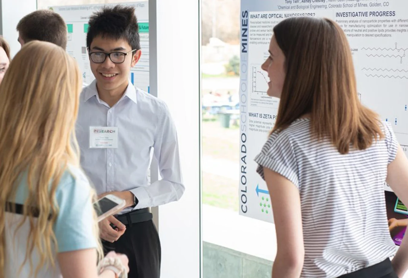 Group of young adults discussing a research poster presentation at Colorado School of Mines in a bright indoor setting.