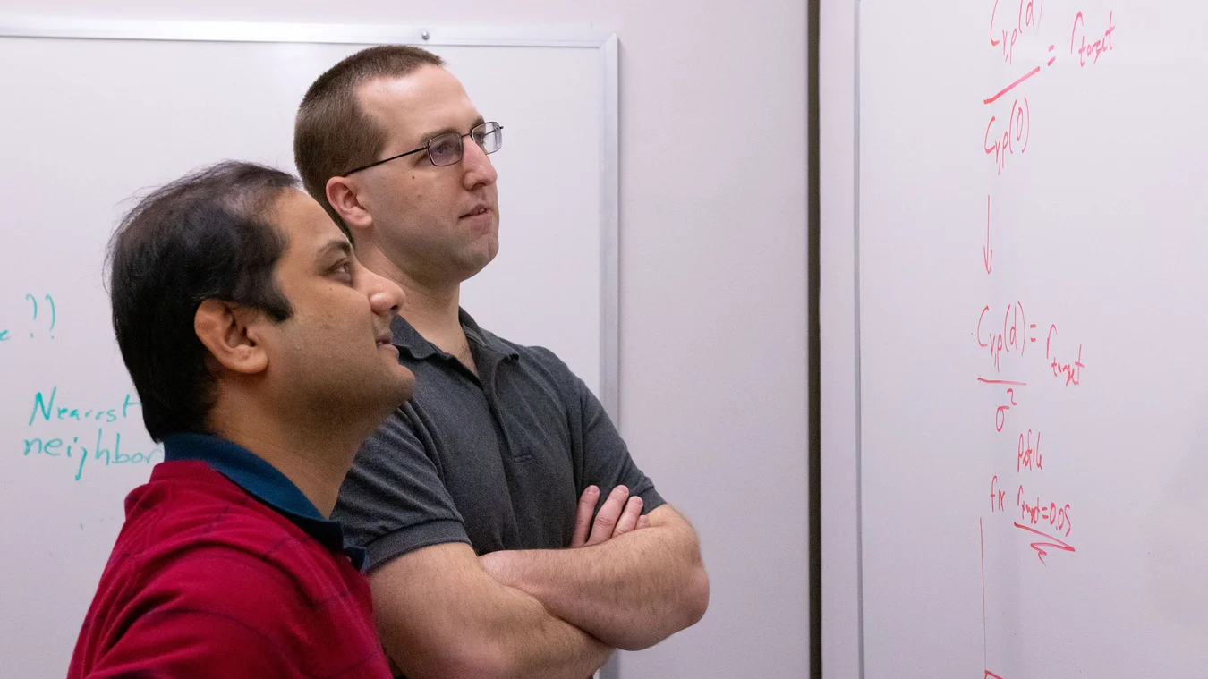 Two men standing next to each other in front of a whiteboard.