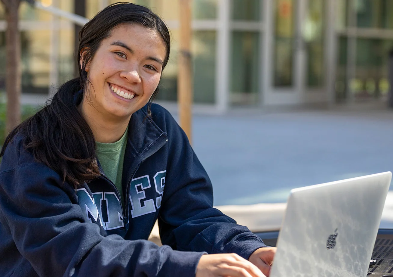 Female Mines student working on a laptop outside a building on campus